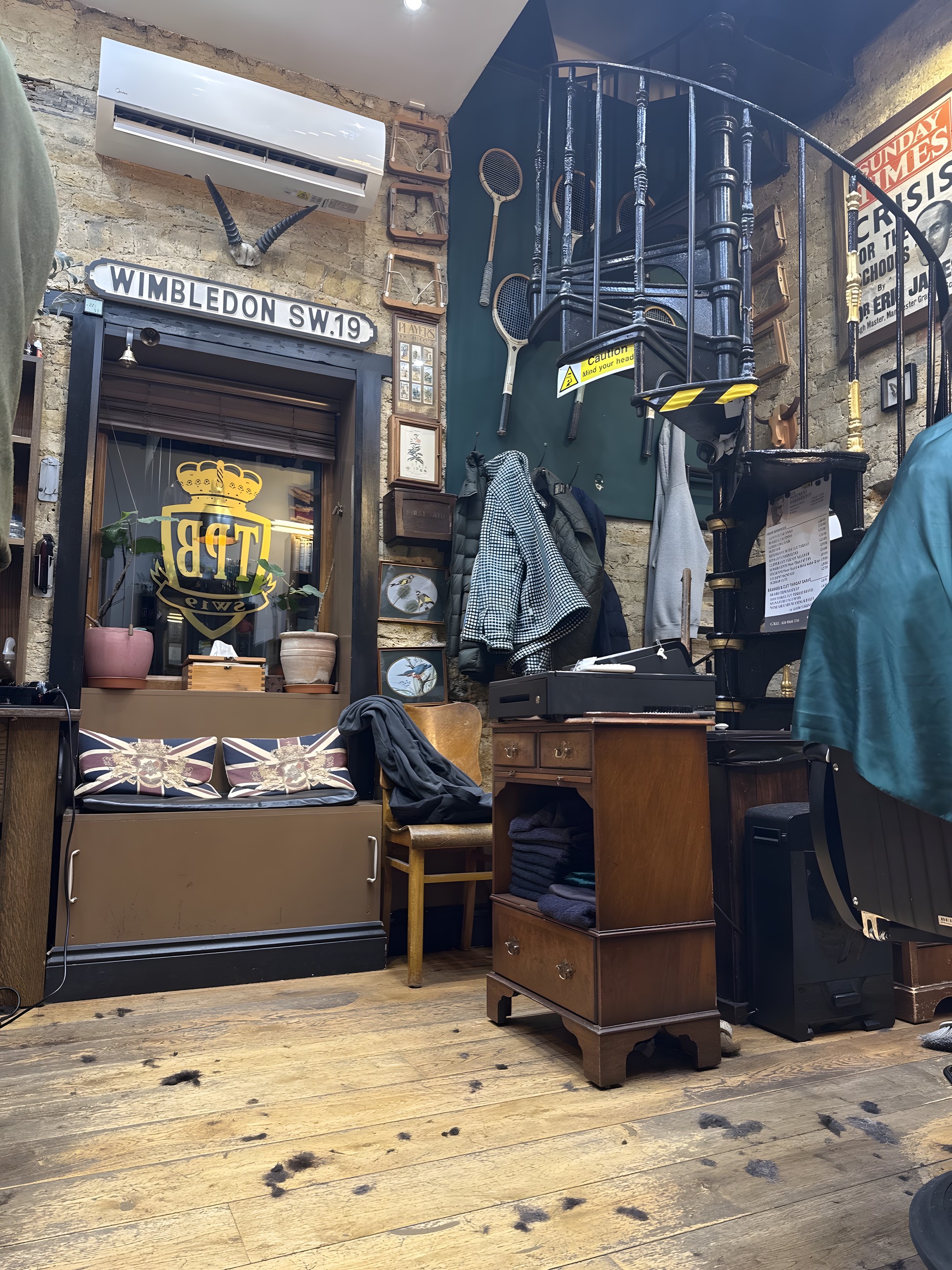Inside the shop: a cast-iron Wimbledon SW.19 street sign and the gold Pavement Barbershop crest above Union Jack cushions
